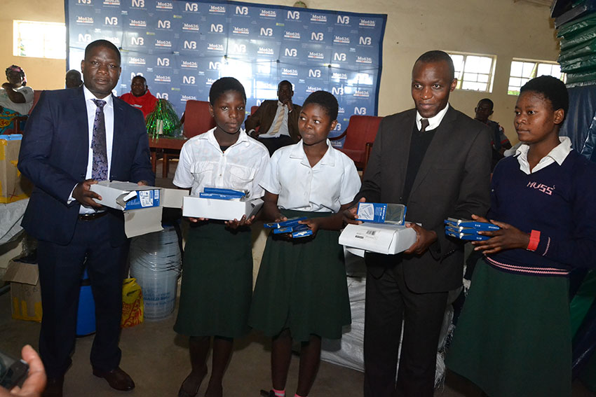 Jiya (left) presenting some educational materials to Namikasi Secondary School girls together with NBM Head of Card and eBanking William Kaunda (second right)